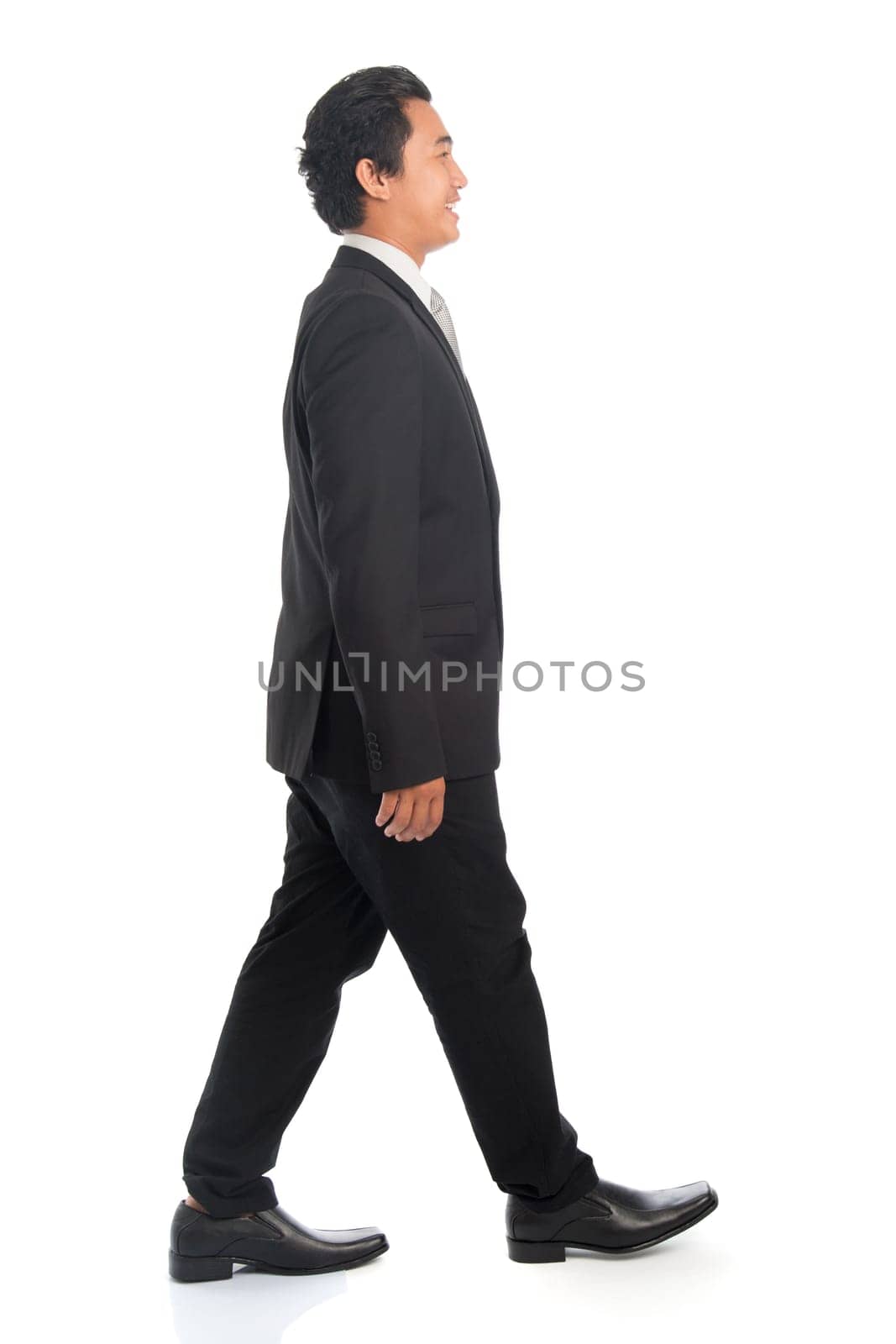 Full length side view of happy young Southeast Asian businessman walking, isolated on white background.