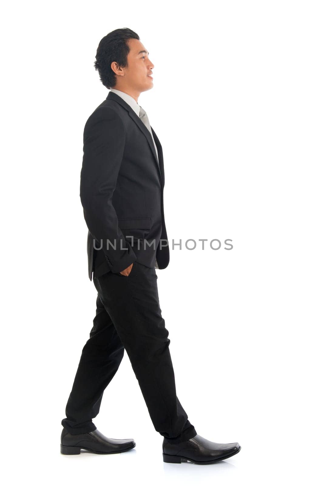 Full length side view of good looking young Southeast Asian businessman walking, isolated on white background.