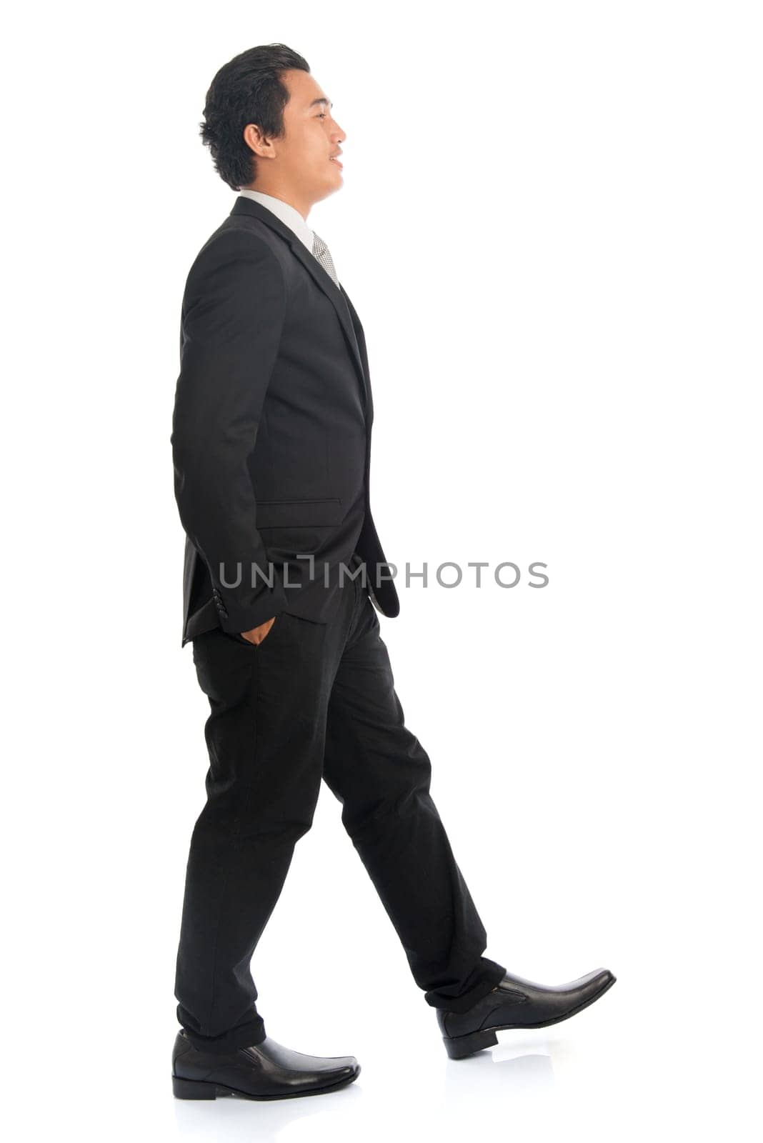 Full body side view of good looking young Southeast Asian businessman walking, isolated on white background.