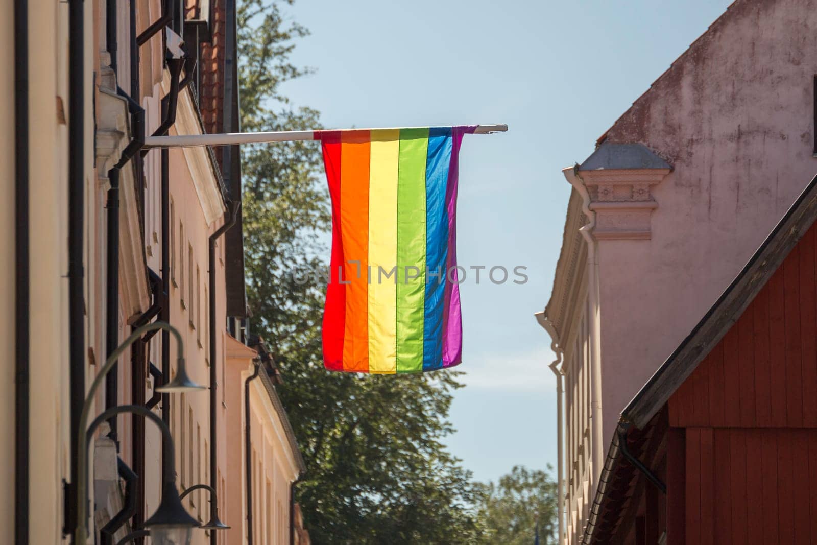 The  Rainbow Flag on a Flagpole by buildings in Visby, Gotland, Sweden.