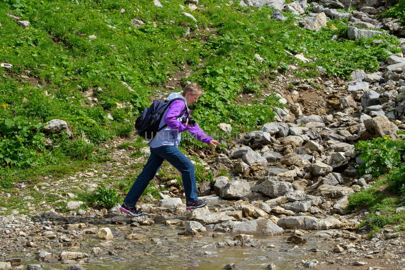 European woman crosses a stream on a hike in the Allgäu
