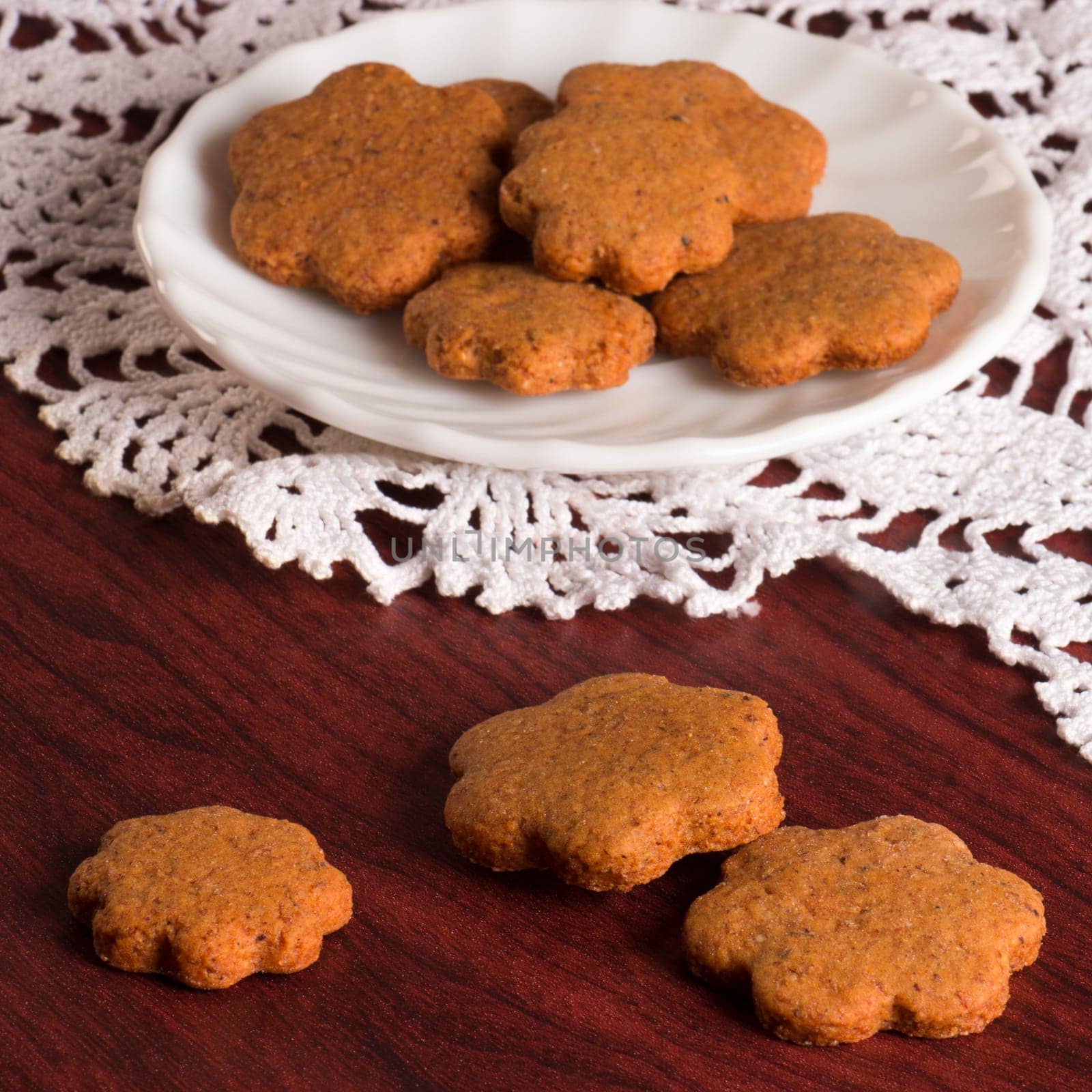 Honey cookies are on crochet tablecloth on wooden background.