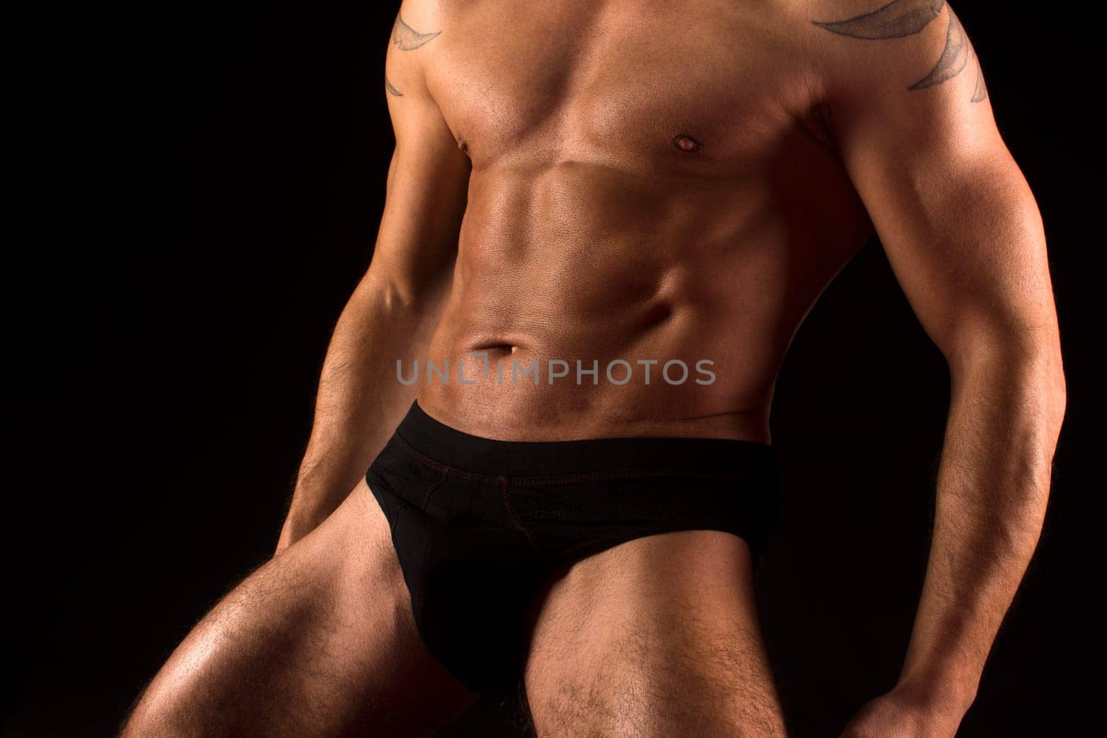 Muscular sexy male body in black underwear on black background.