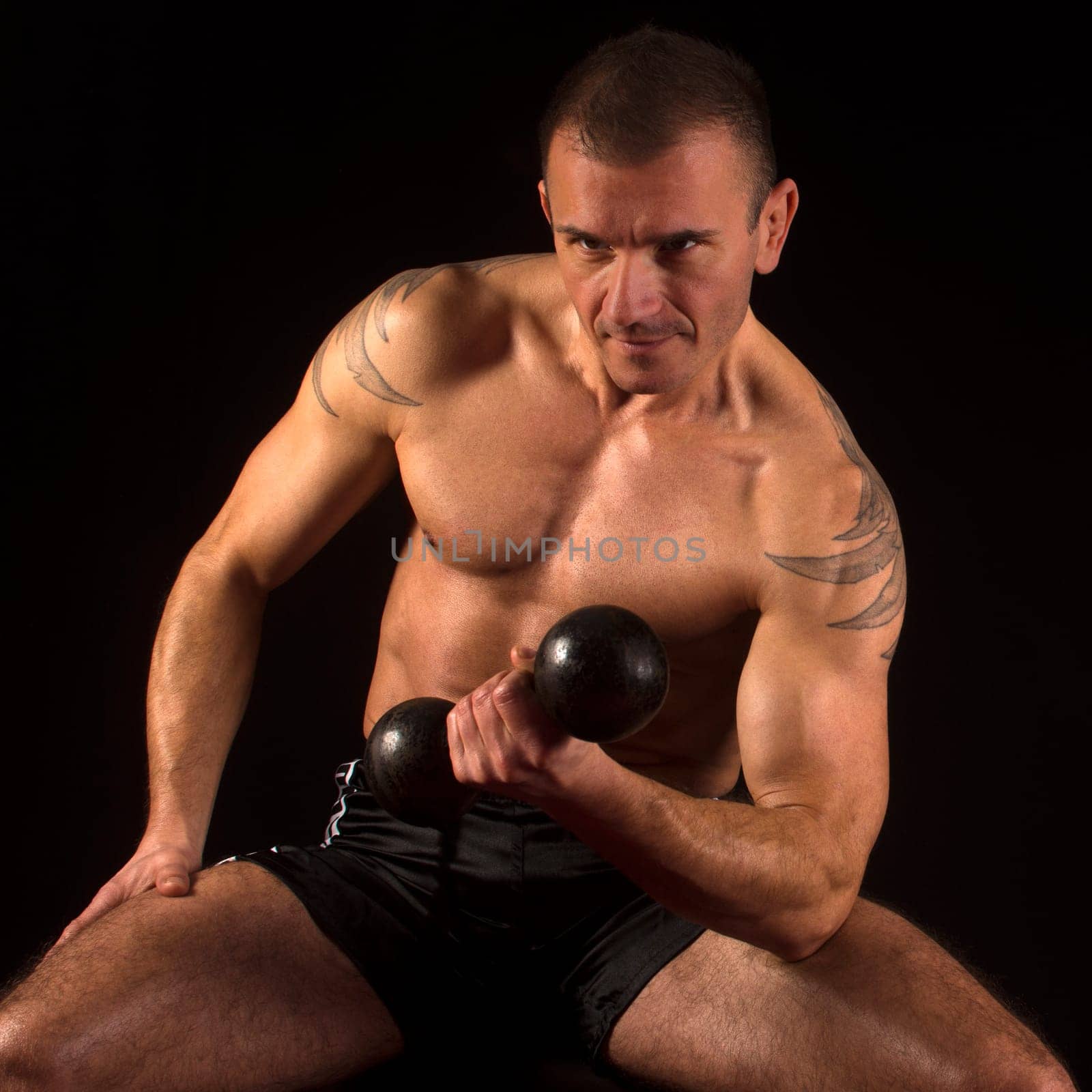 Muscular man trains his biceps with weight on black background.