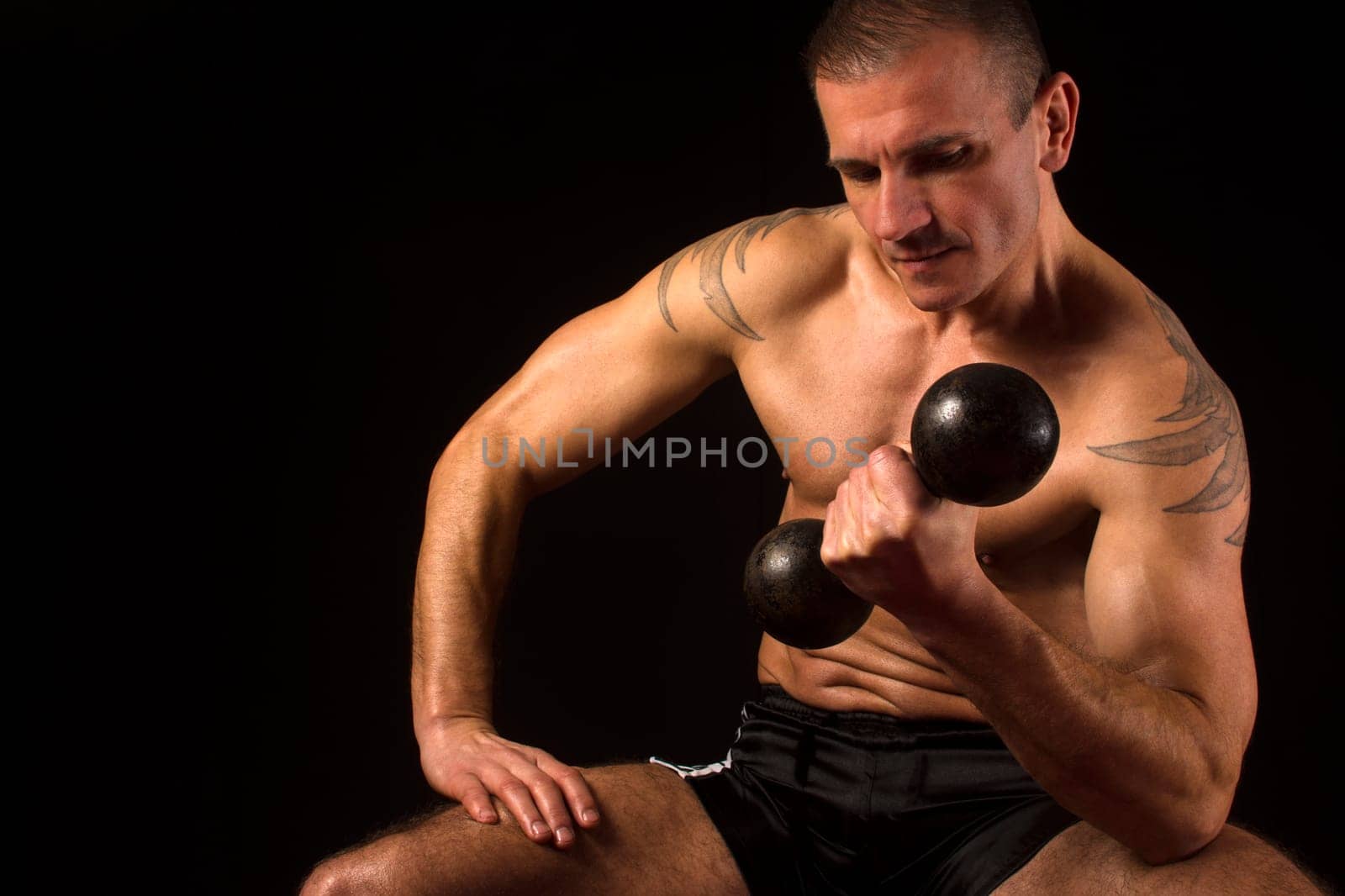 Man exercise his biceps with weight on black background.