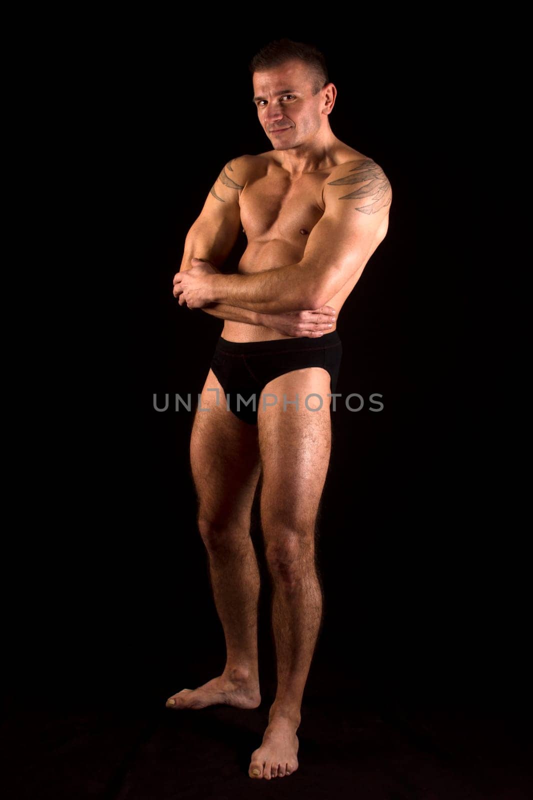 The man is standing in underwear on black background.