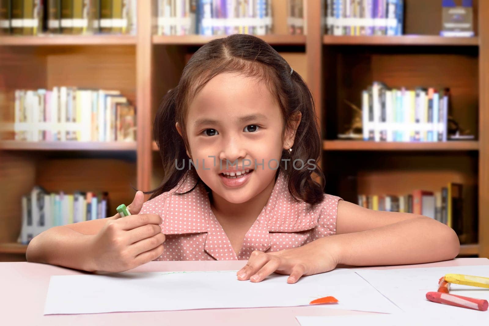 Smiling asian cute little girl drawing with crayon on the classroom