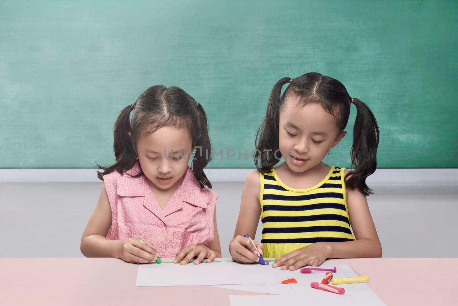 Pretty asian children drawing together on sheet of paper against chalkboard background