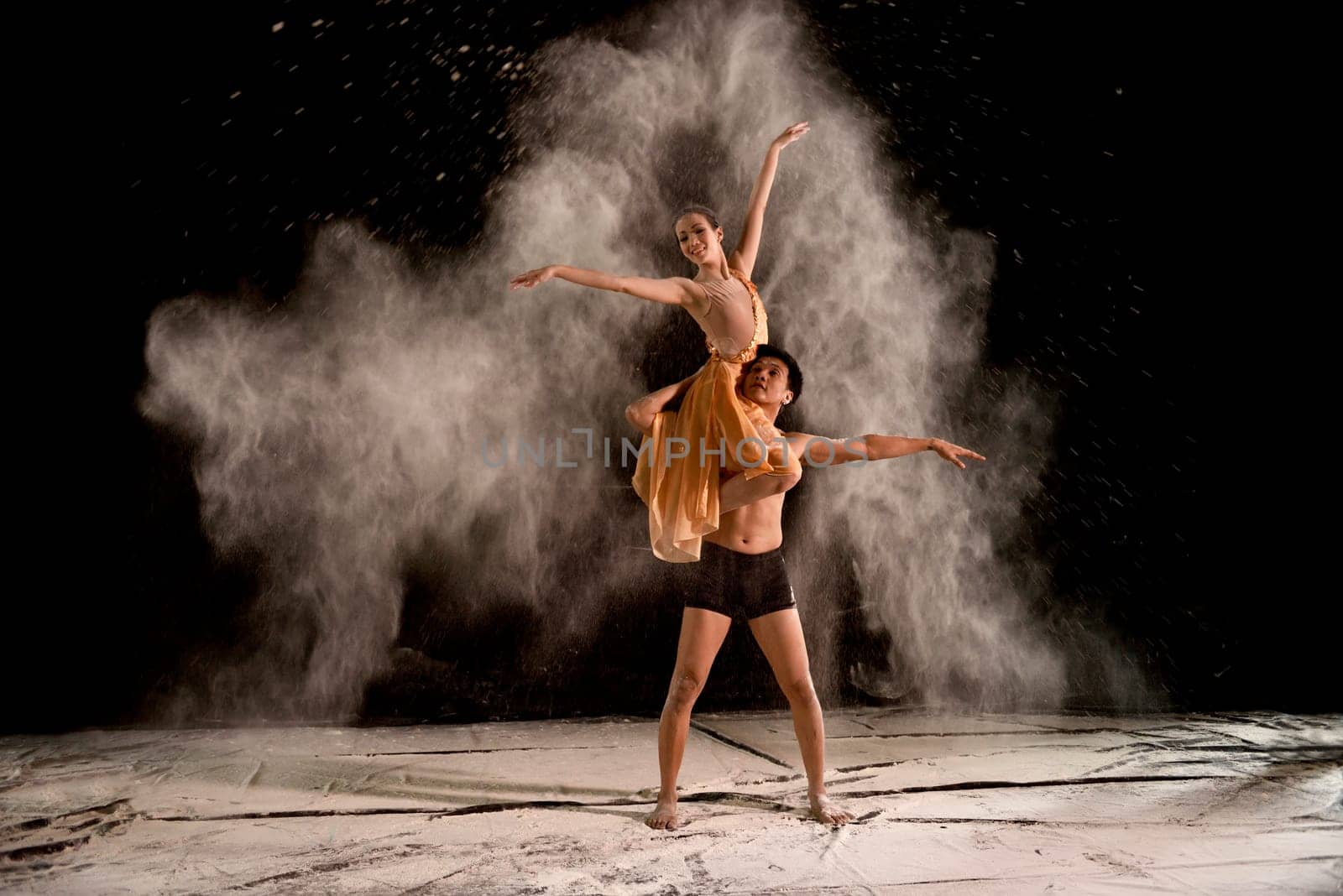 Attractive couple ballet dancer with white powder in the air against black background