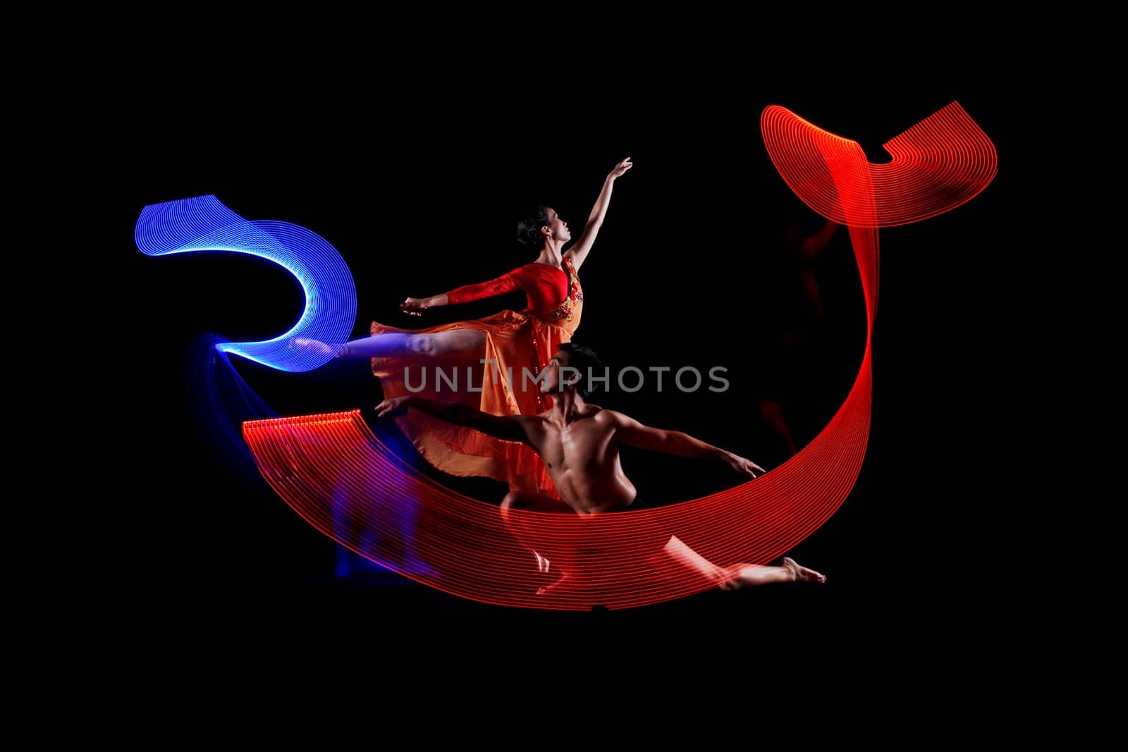 Portrait of couple ballet dancing with motion lights effect over black background