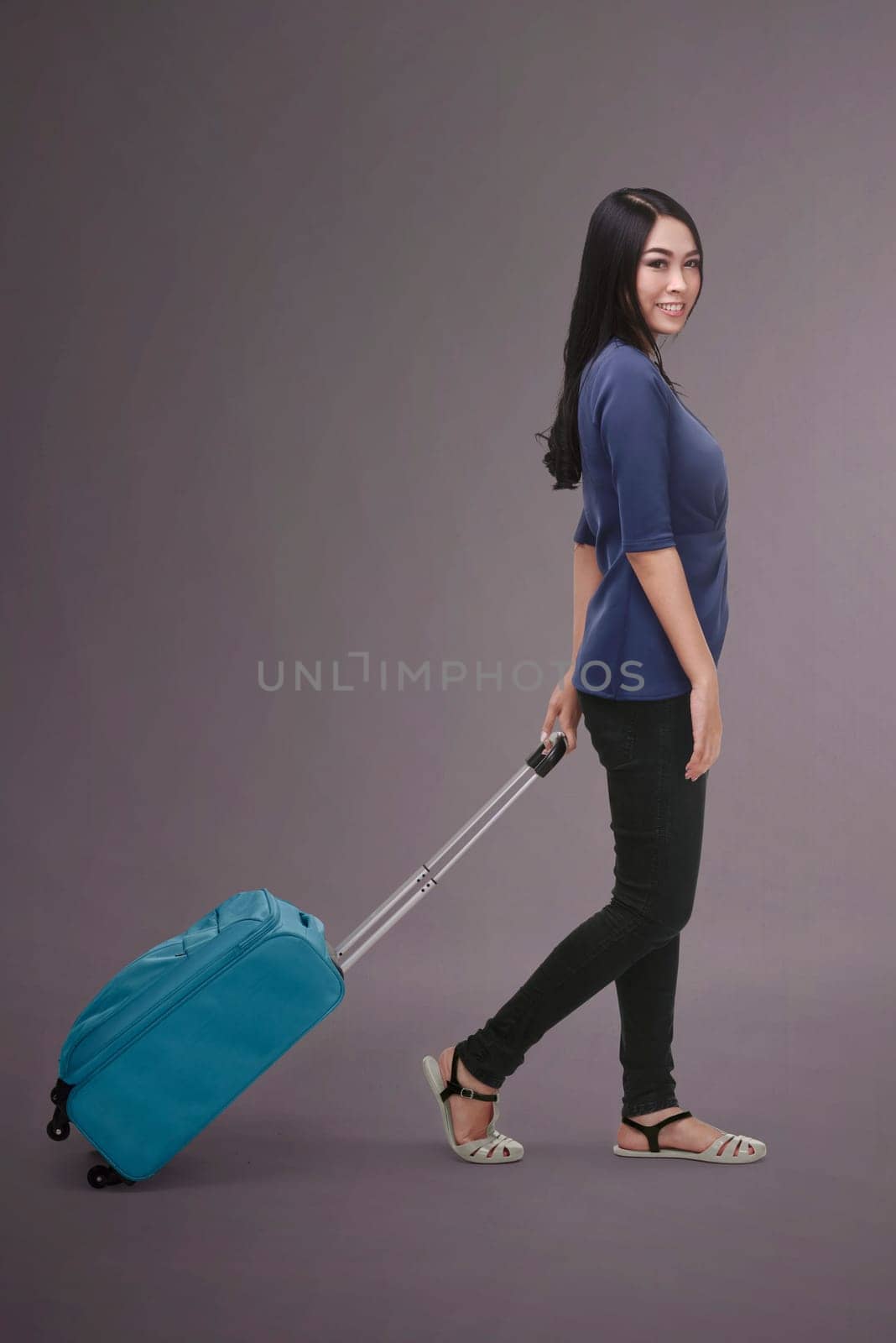 Pretty asian traveler woman carrying suitcase against dark background