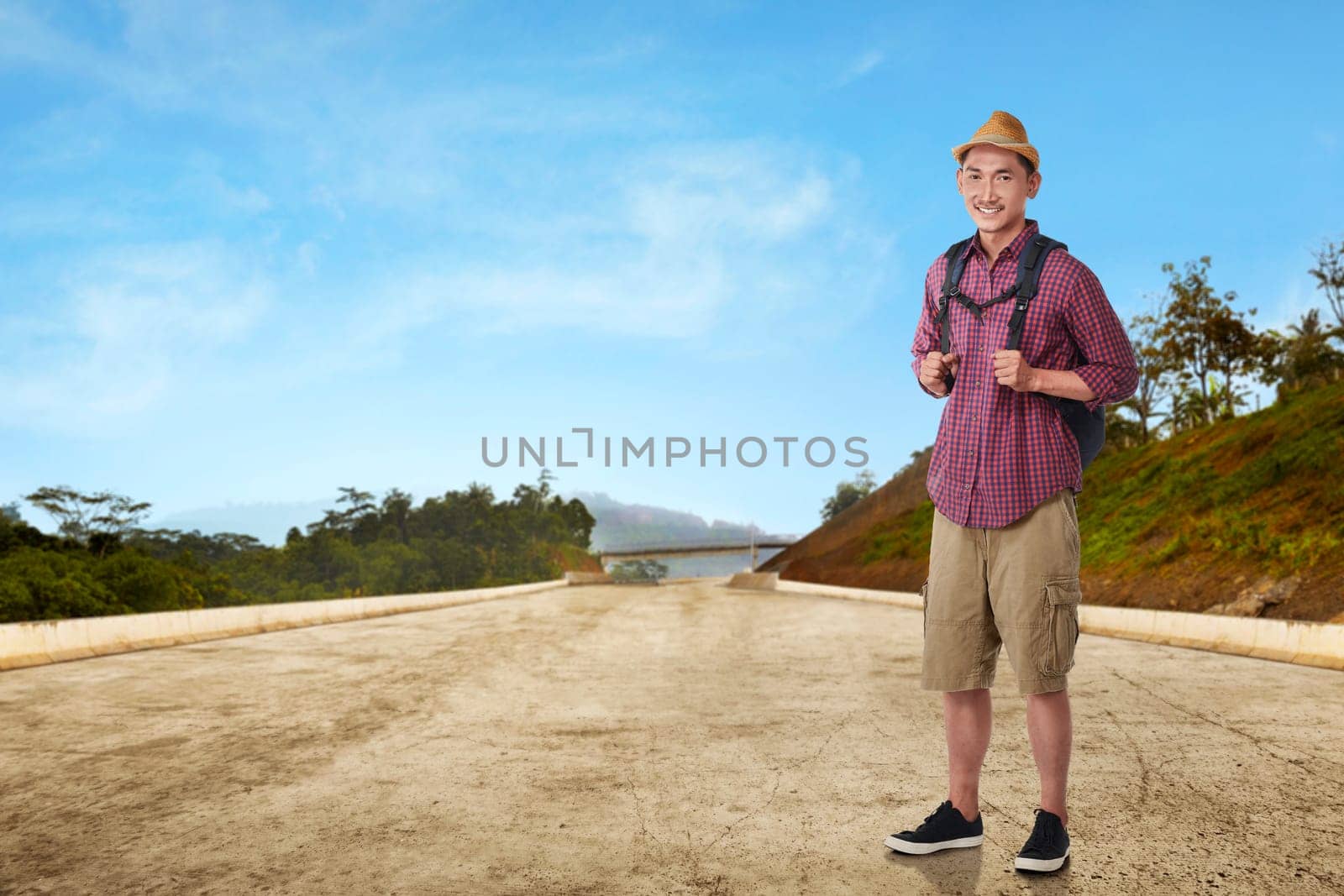 Young asian man traveling with hat and bag against landscape background