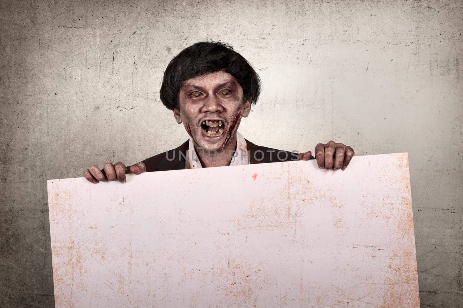 Creepy and bloody asian zombie man holding empty banner over dirty wall background