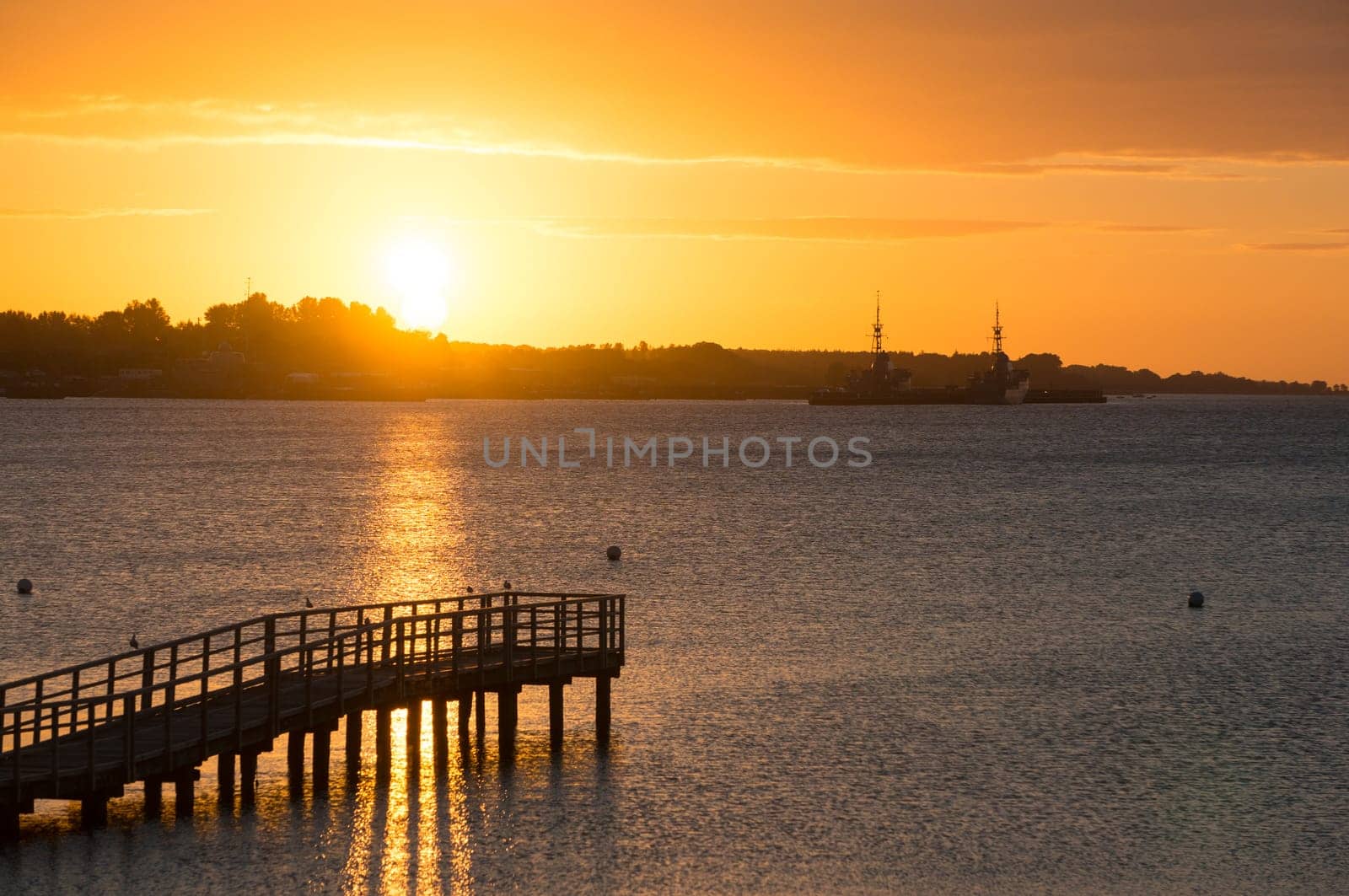 Beautiful sunrise in the summer over old wooden bridge and silent glossy sea. Sunrise over the sea. Pier on the foreground. Panorama