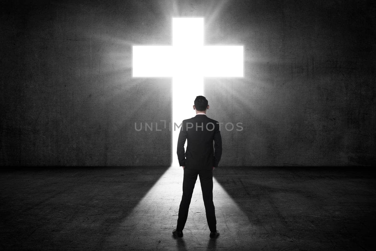 Business man looking the shining cross on the wall. Religious concept