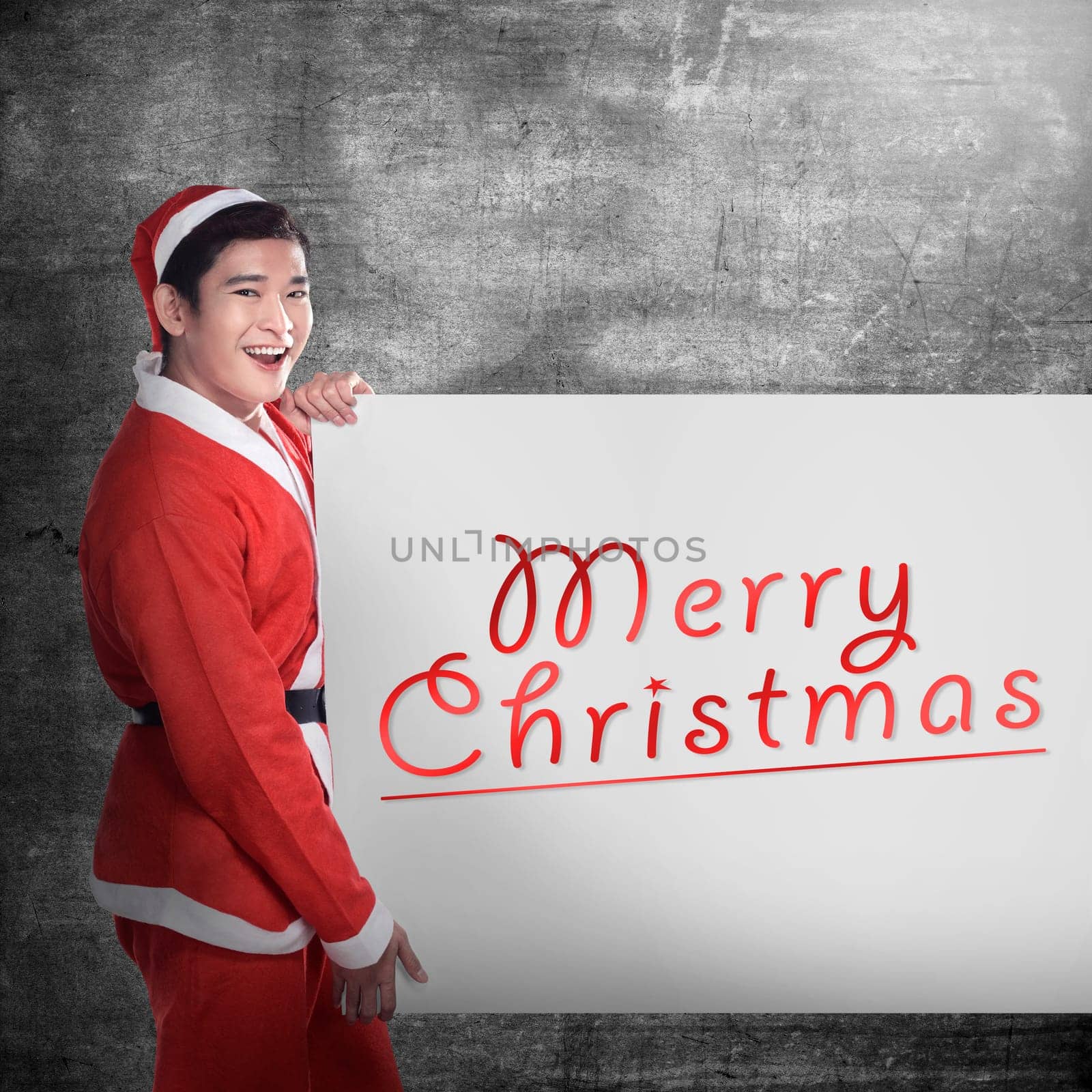 Asian man wearing santa claus costume holding banner with merry christmas writing