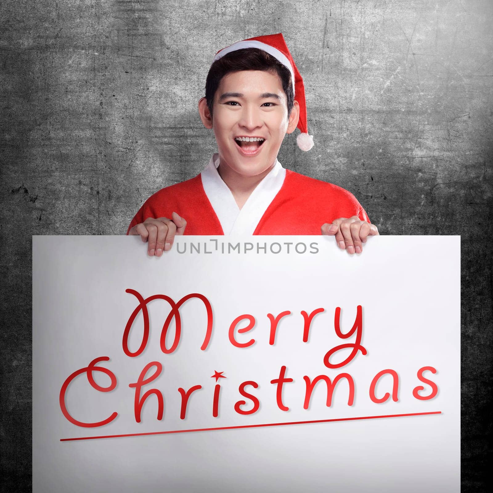 Asian man wearing santa claus costume holding banner with merry christmas writing