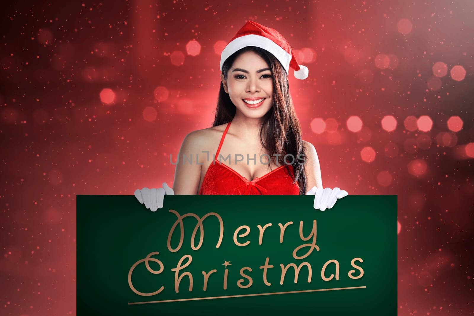 Young attractive asian woman wearing Santa Claus costume holding billboard with merry christmas writing