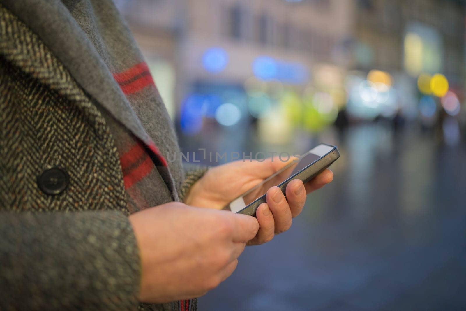 Close up of males hands texting on mobile phone outdoors on the highstreet during winter.