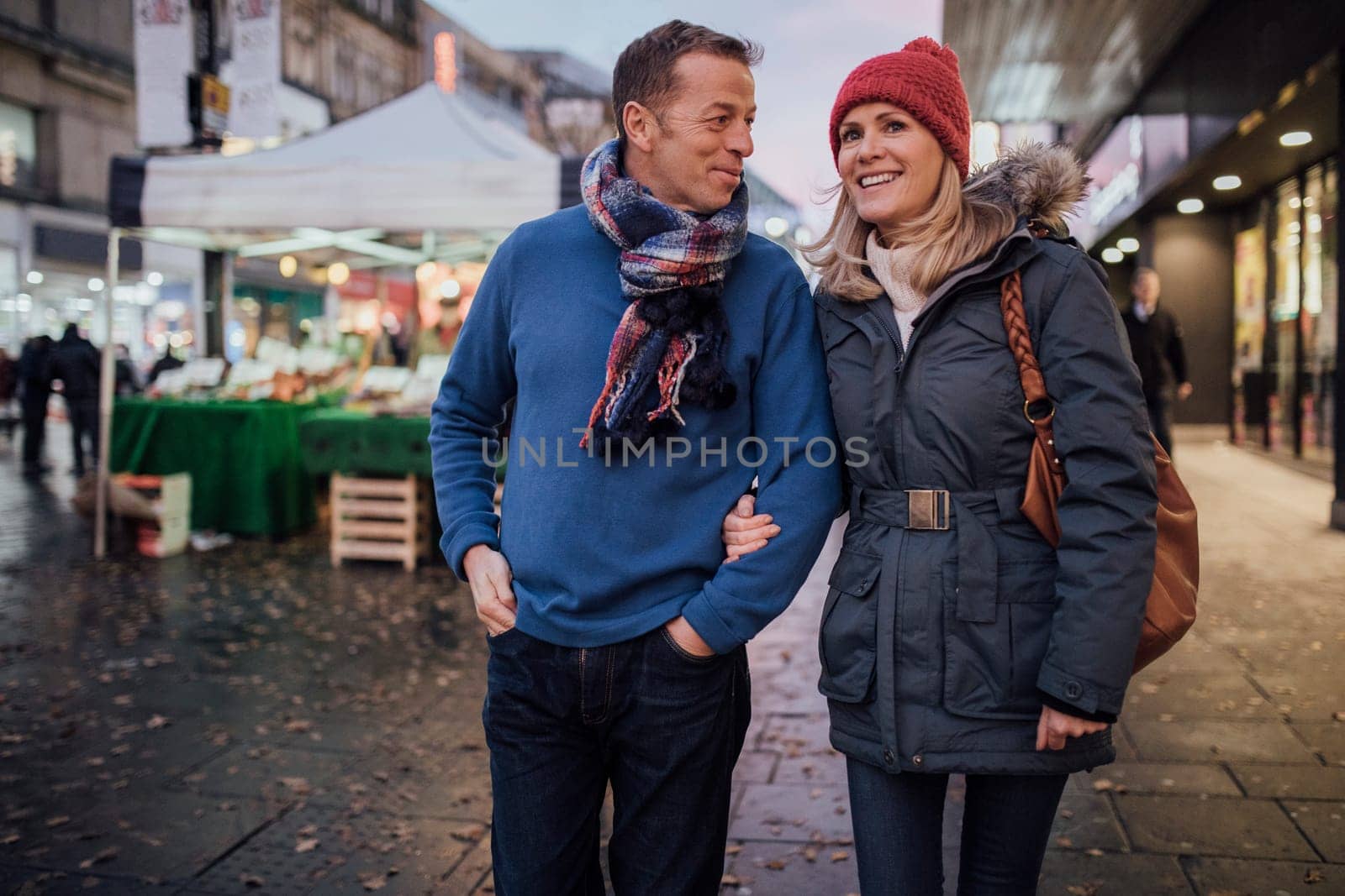 Mature coup le are enjoying an evening stroll through the city christmas market.