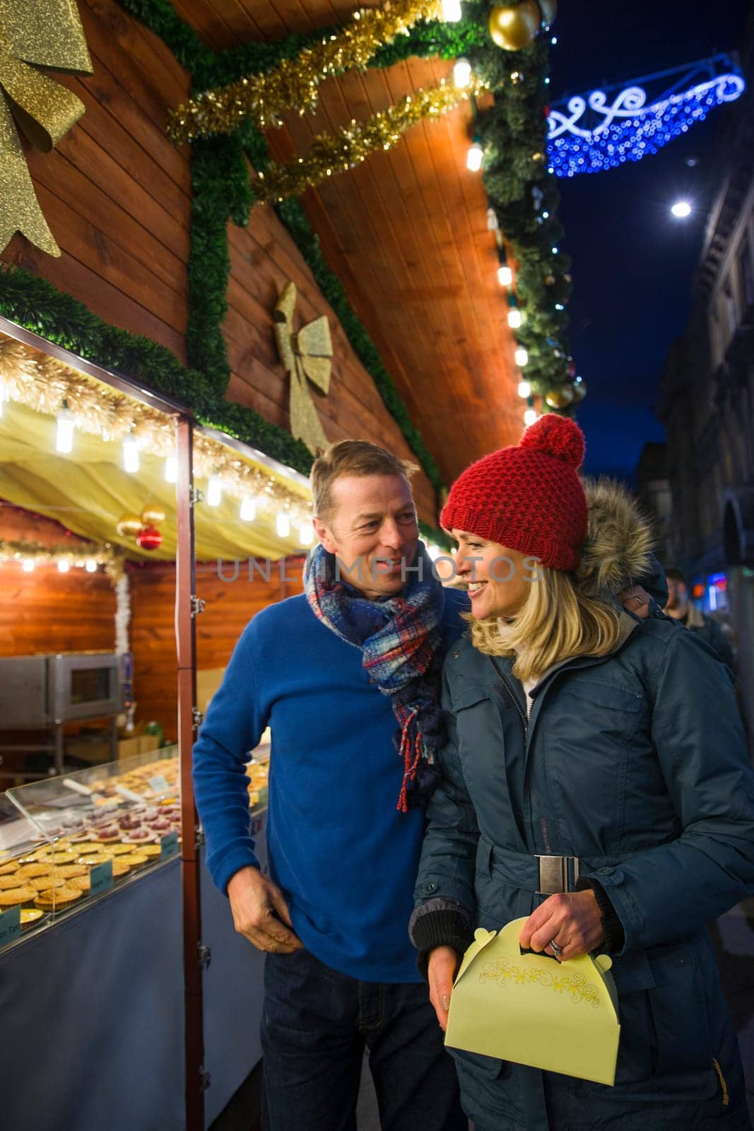 Mature couple are looking at a french pattisserie stall together in the city christmas market.