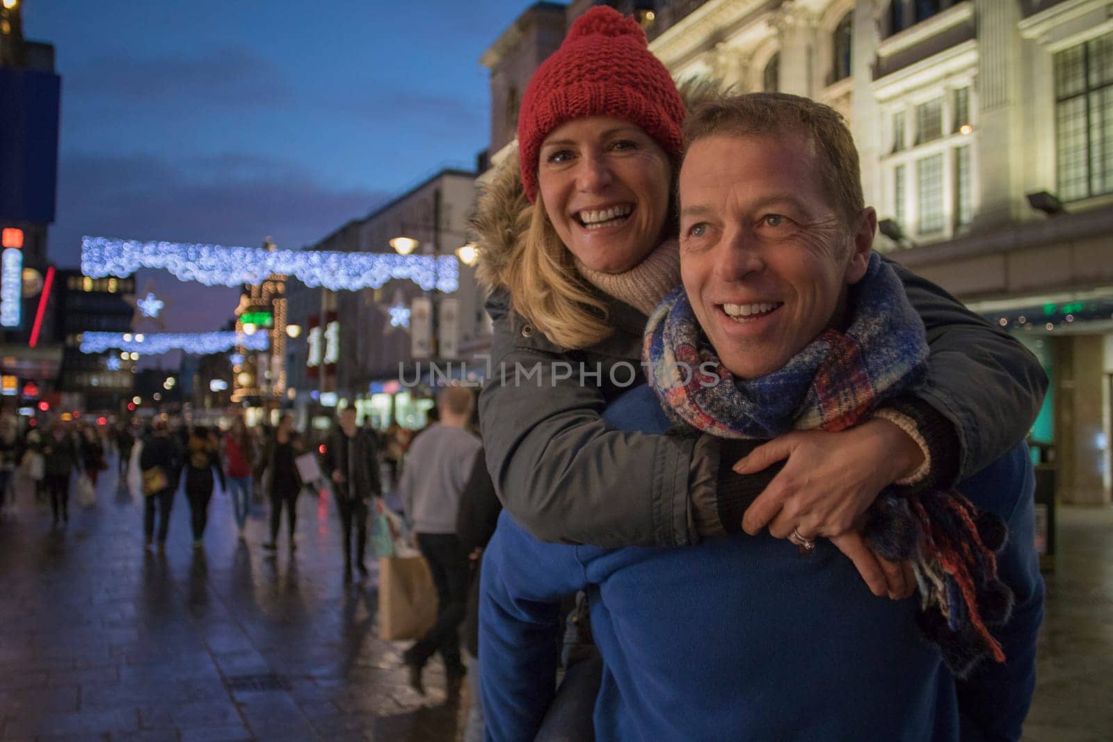 Mature man is giving his wife a piggy back through the city centre at Christmas time.