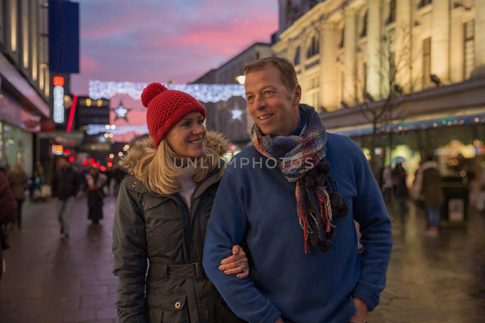 Mature couple are enjoying an evening stroll through town at Christmas time.