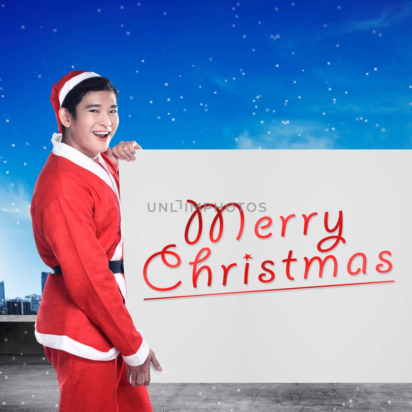 Asian man wearing santa claus costume holding banner with merry christmas writing