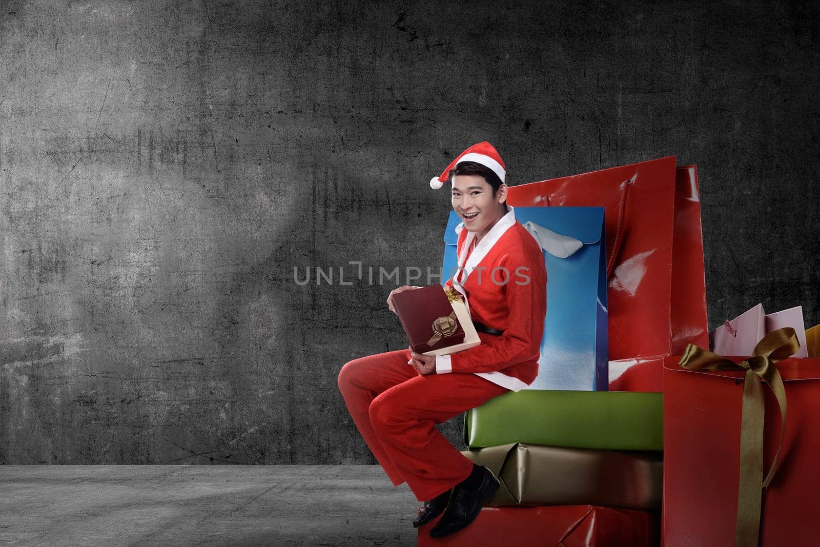 Young asian man wearing santa claus costume sit on the big present box