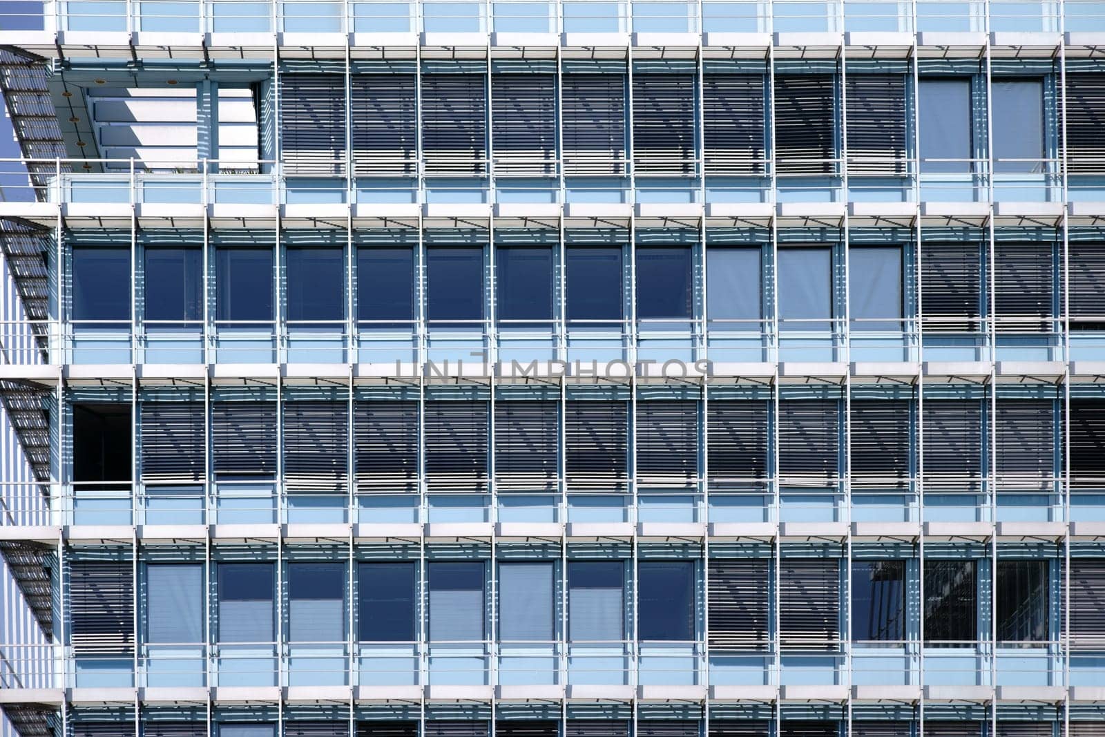The modern façade of an office building with rows of windows and metal blinds.