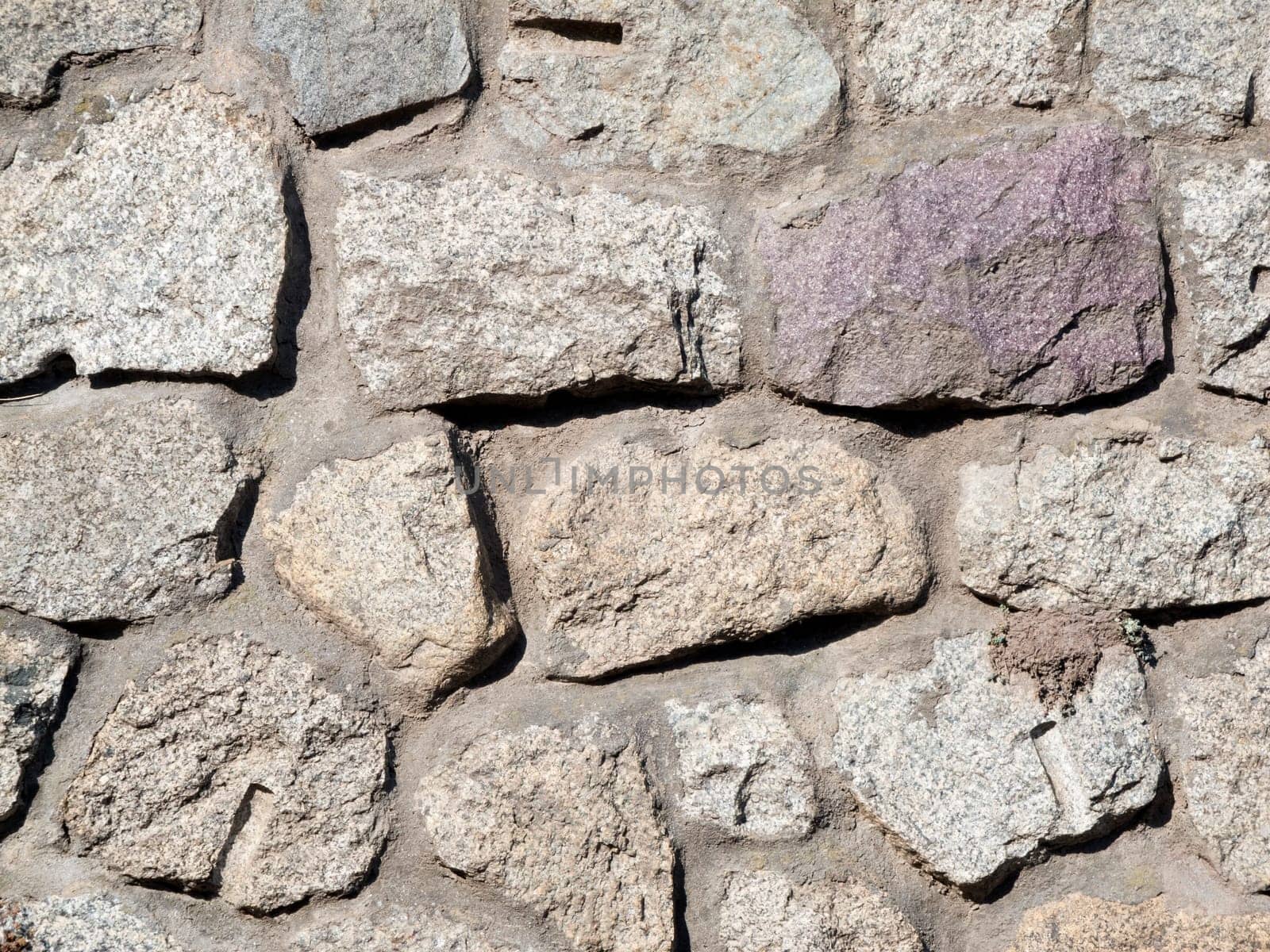 Format-filling view of irregular granite stones as a masonry wall with joints.