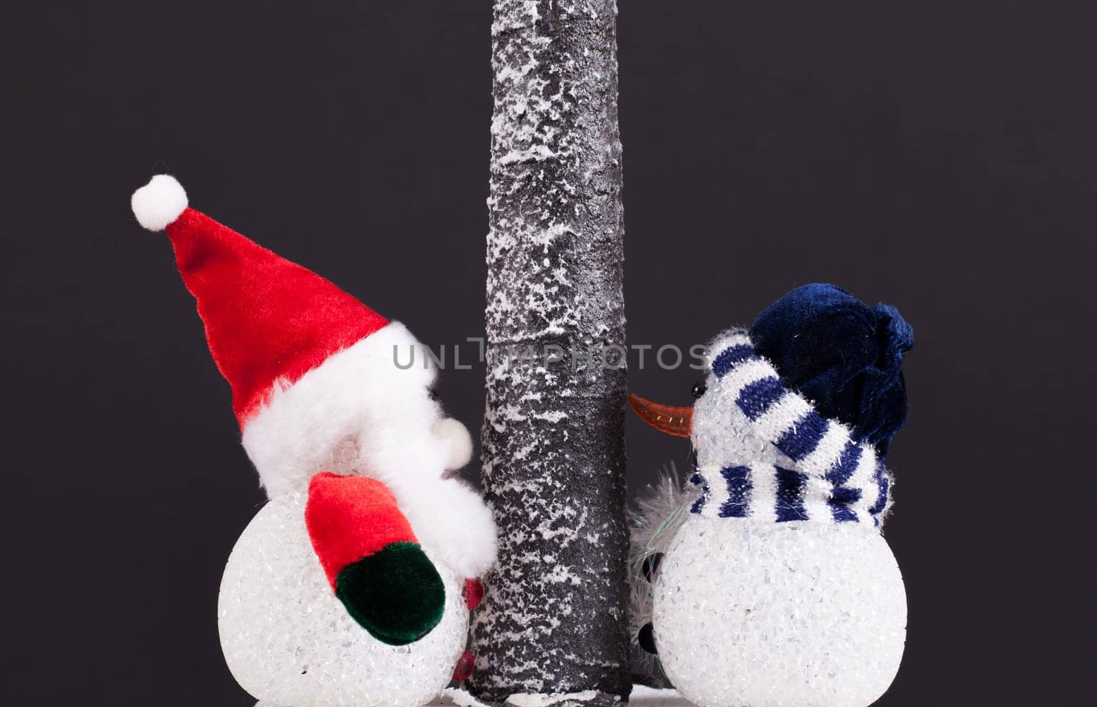 Toy Father Christmas and snowman under a tree. Festive scene on a black background