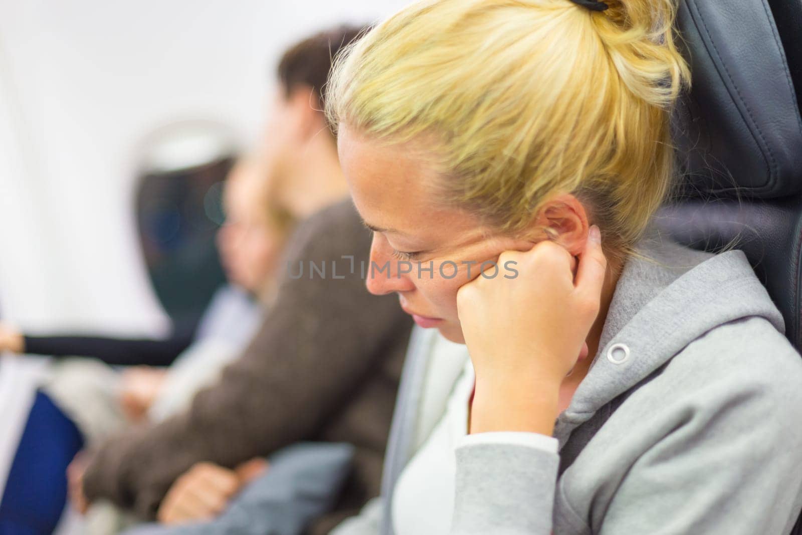 Tired blonde casual caucasian lady napping on seat while traveling by airplane. Commercial transportation by planes.
