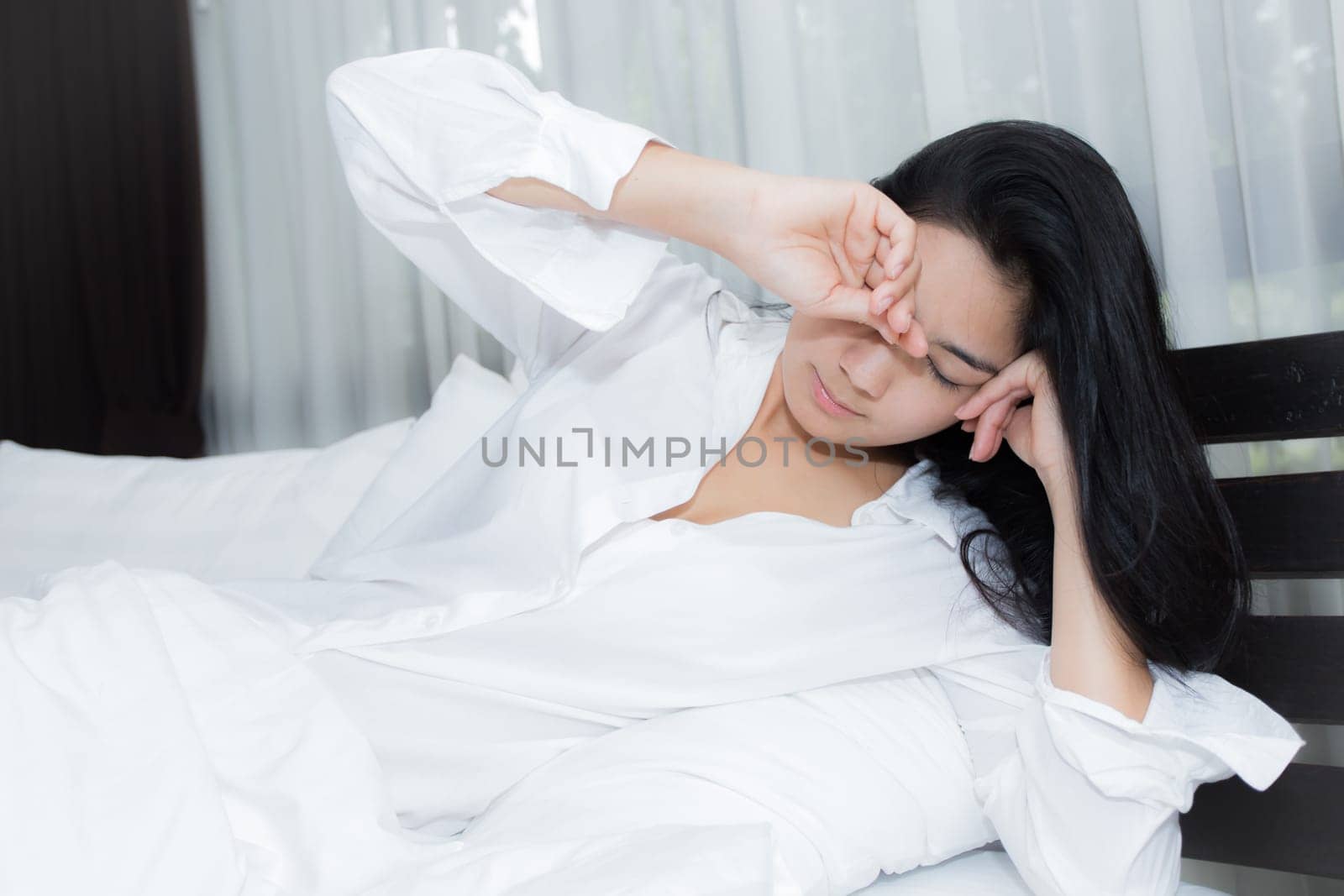 Young Asian woman playing puppy doll on the bed in morning bedroom, alone and lonely