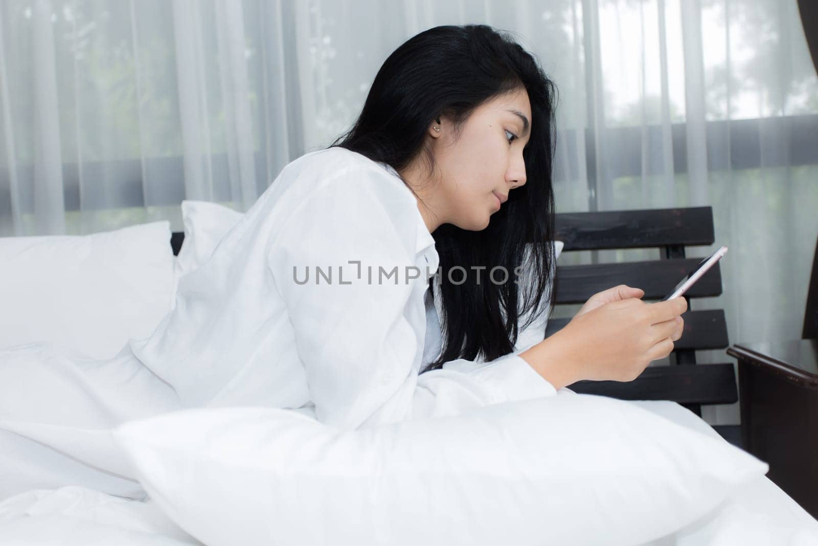Young Asian woman playing puppy doll on the bed in morning bedroom, alone and lonely