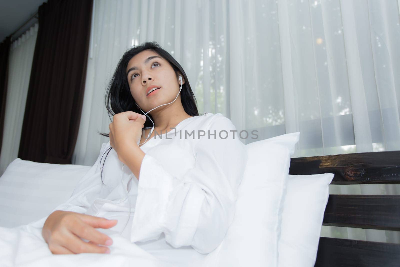 Young Asian woman playing puppy doll on the bed in morning bedroom, alone and lonely
