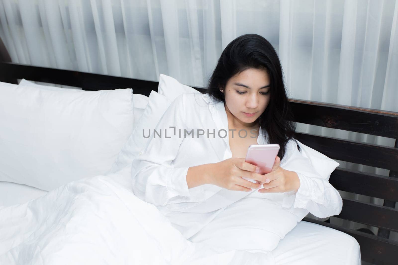 Young Asian woman playing puppy doll on the bed in morning bedroom, alone and lonely