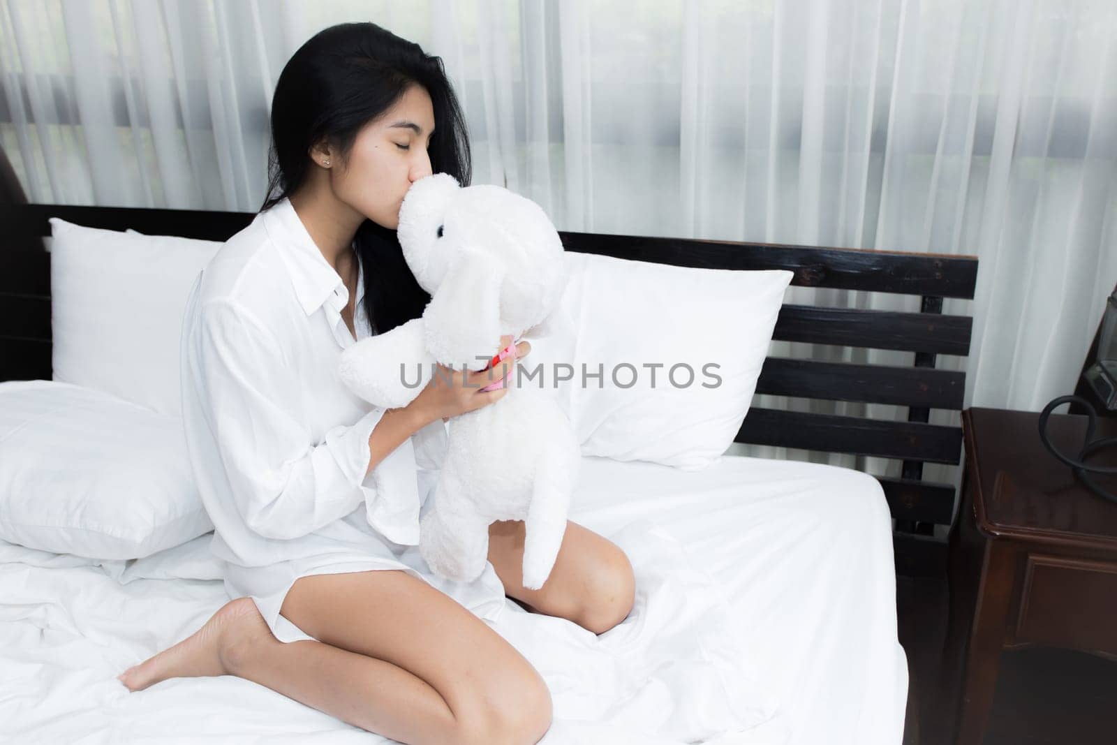 Young Asian woman playing puppy doll on the bed in morning bedroom, alone and lonely