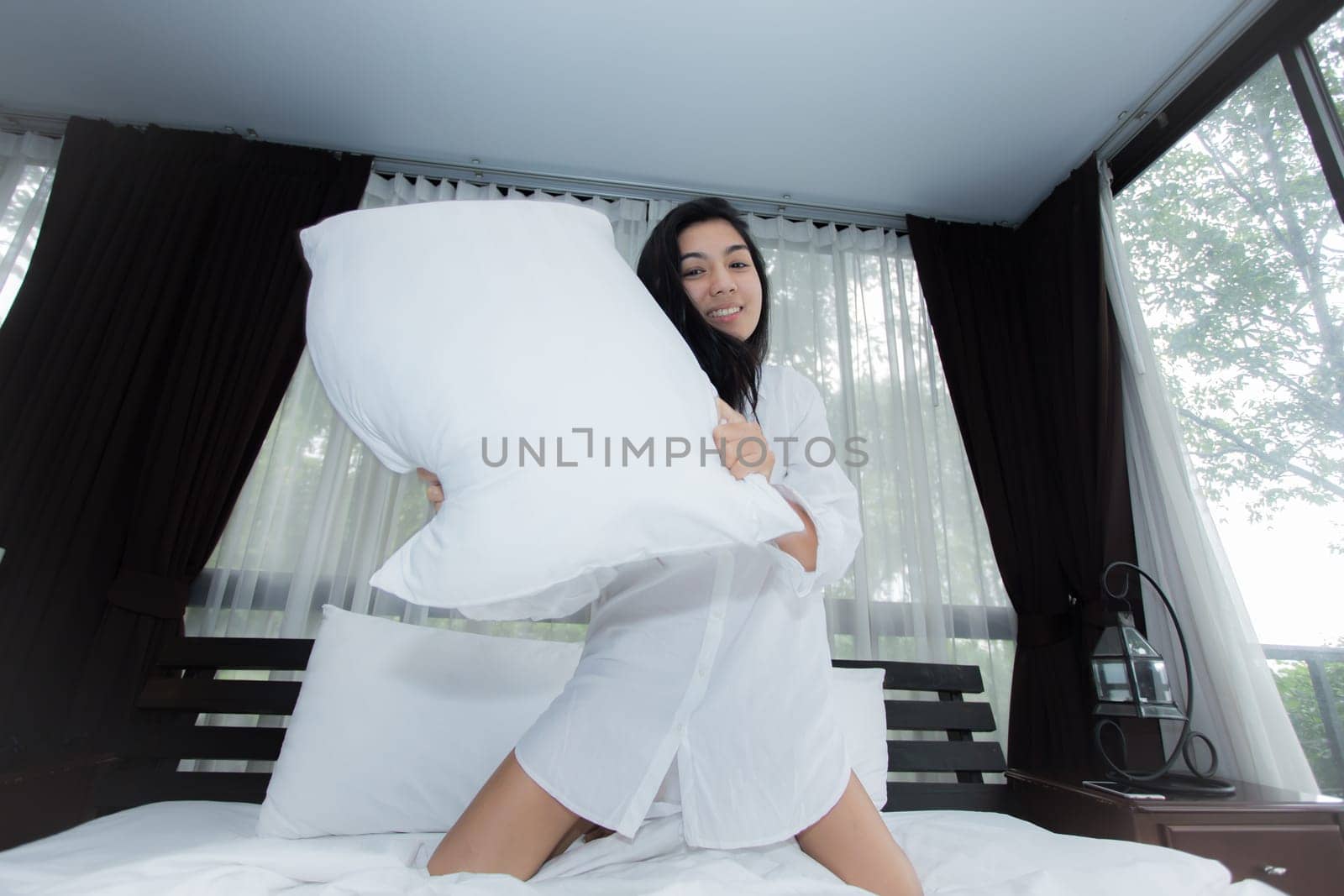 Young Asian woman playing puppy doll on the bed in morning bedroom, alone and lonely