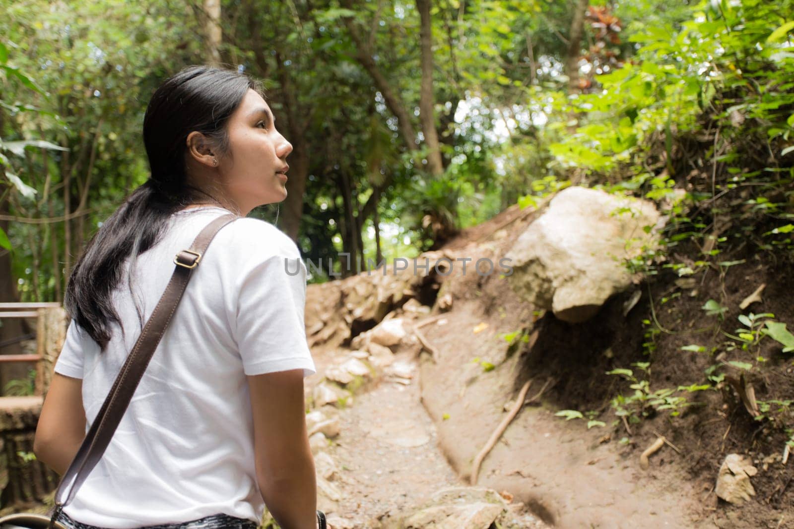 Young asian woman hiker stops to tie her shoe on a summer hiking trail in forest.