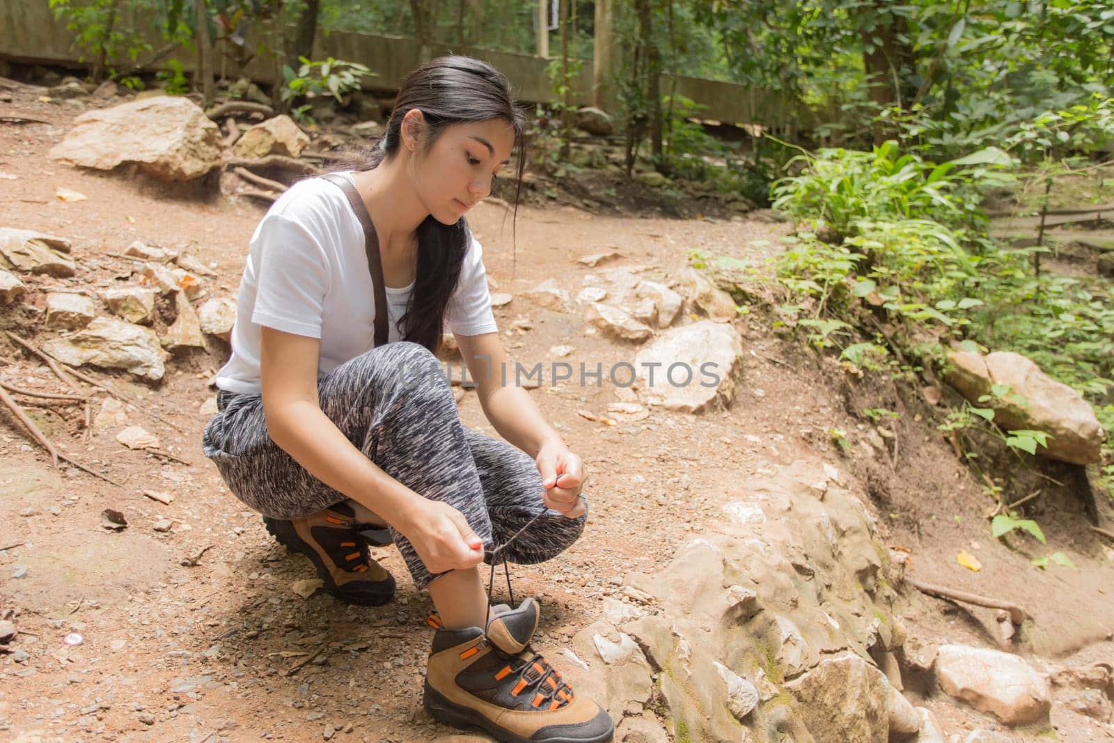 Young asian woman hiker stops to tie her shoe on a summer hiking trail in forest.