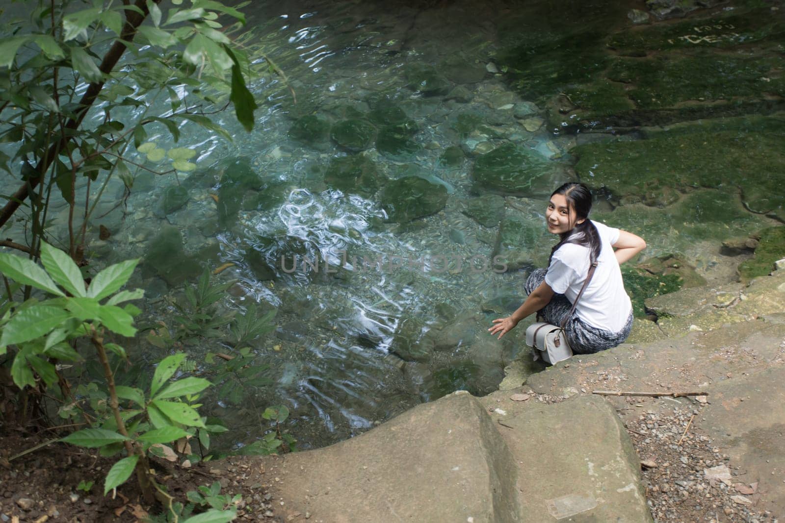 Young asian woman hiker stops to tie her shoe on a summer hiking trail in forest.