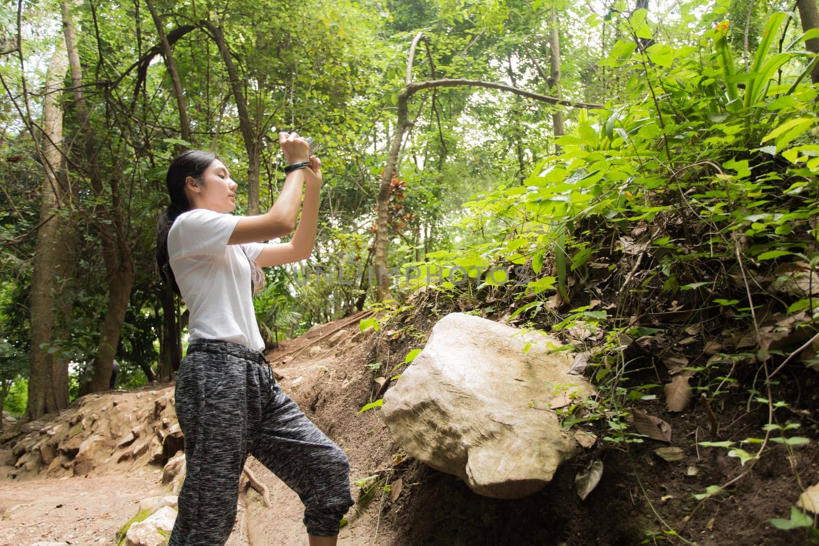 Young asian woman hiker stops to tie her shoe on a summer hiking trail in forest.