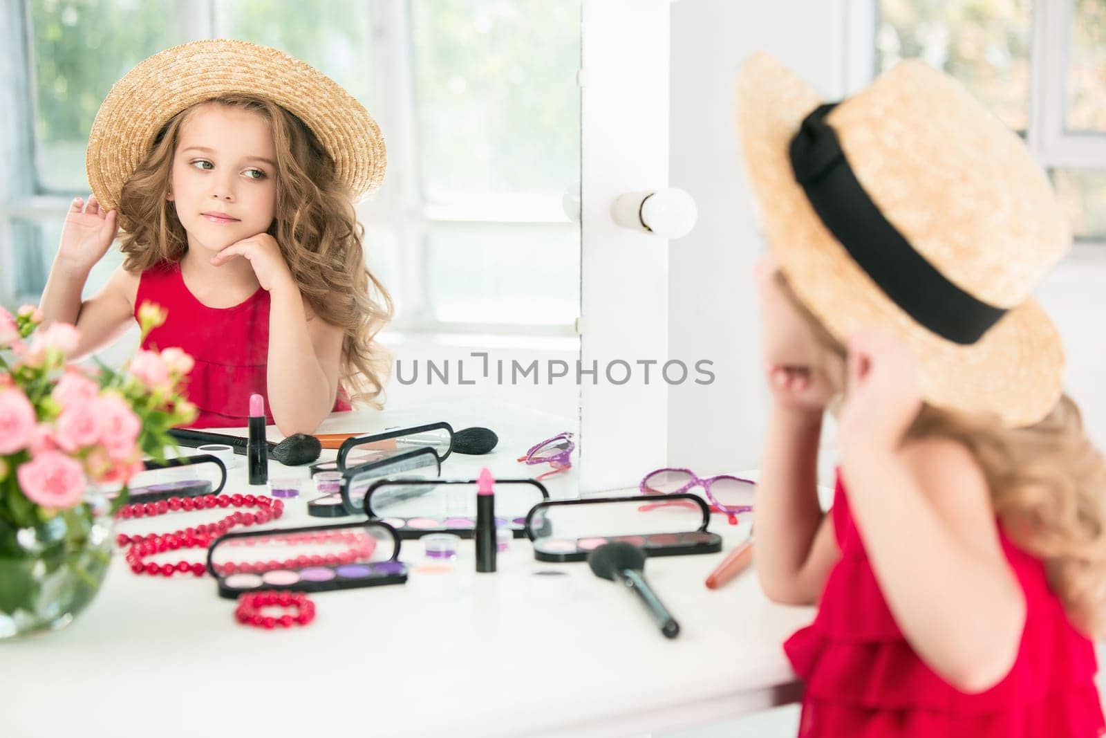 A little girl with red dress and cosmetics. She is in mother's bedroom, sitting near the mirror.
