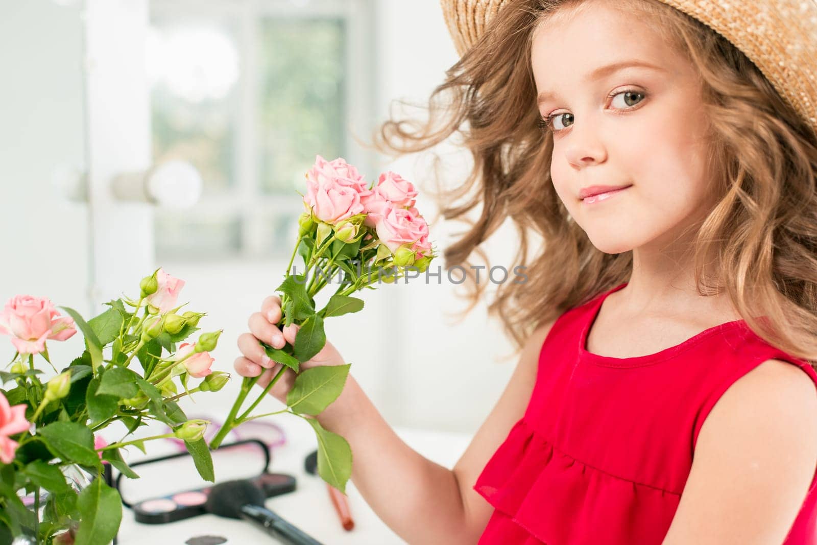 A little girl with red dress and cosmetics. She is in mother's bedroom, sitting near the mirror.