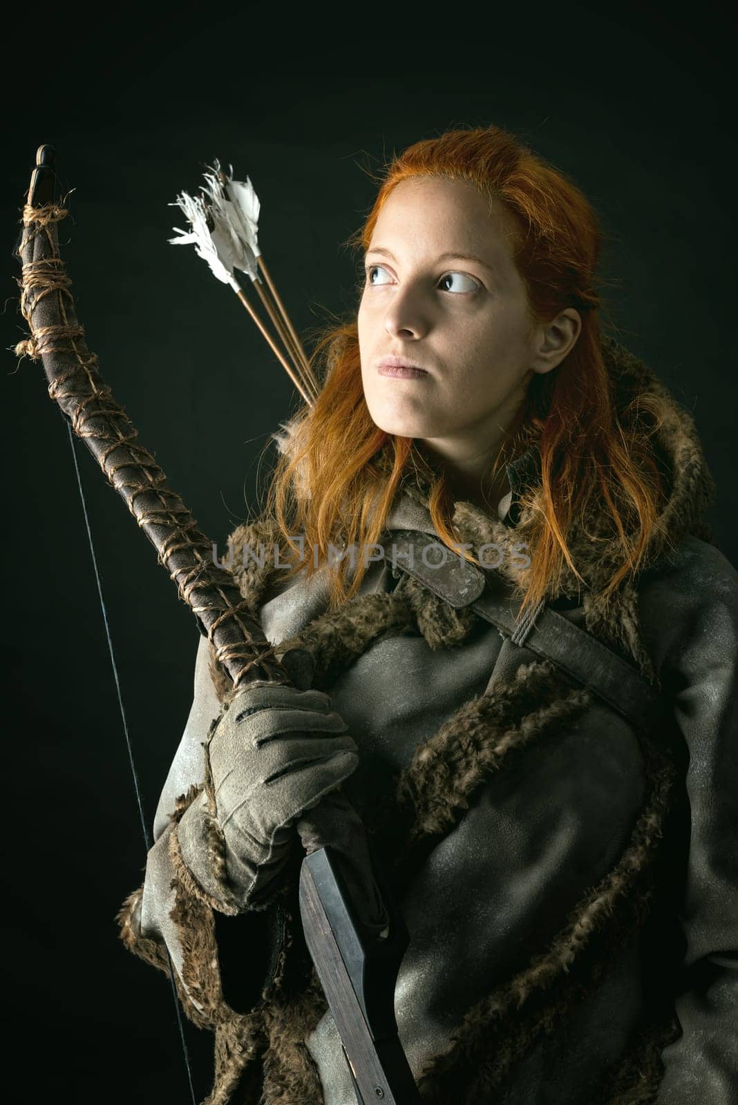 girl archer in a costume with bow isolated in a dark background