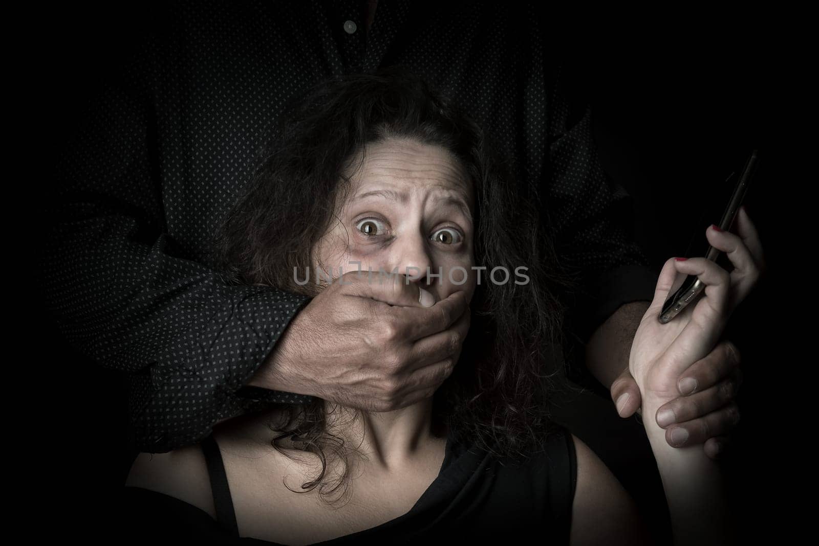 Abused woman trying to call for help with husband covering her mouth, victim of domestic violence