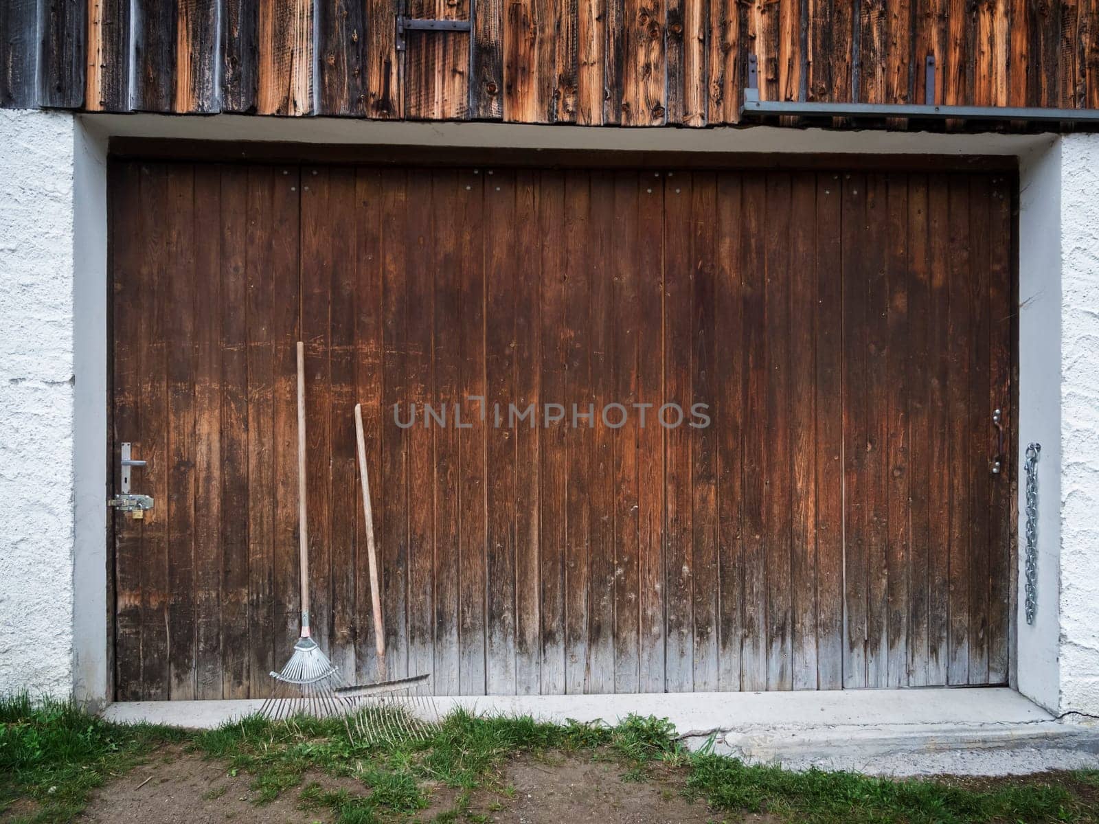 Frontal view of a wide wooden garage door with two leaning rakes.