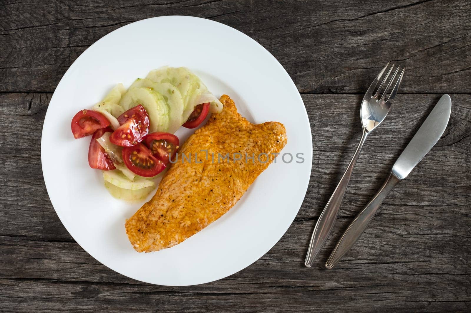 Fried turkey schnitzel with cucumber salad and tomatoes on a plate
