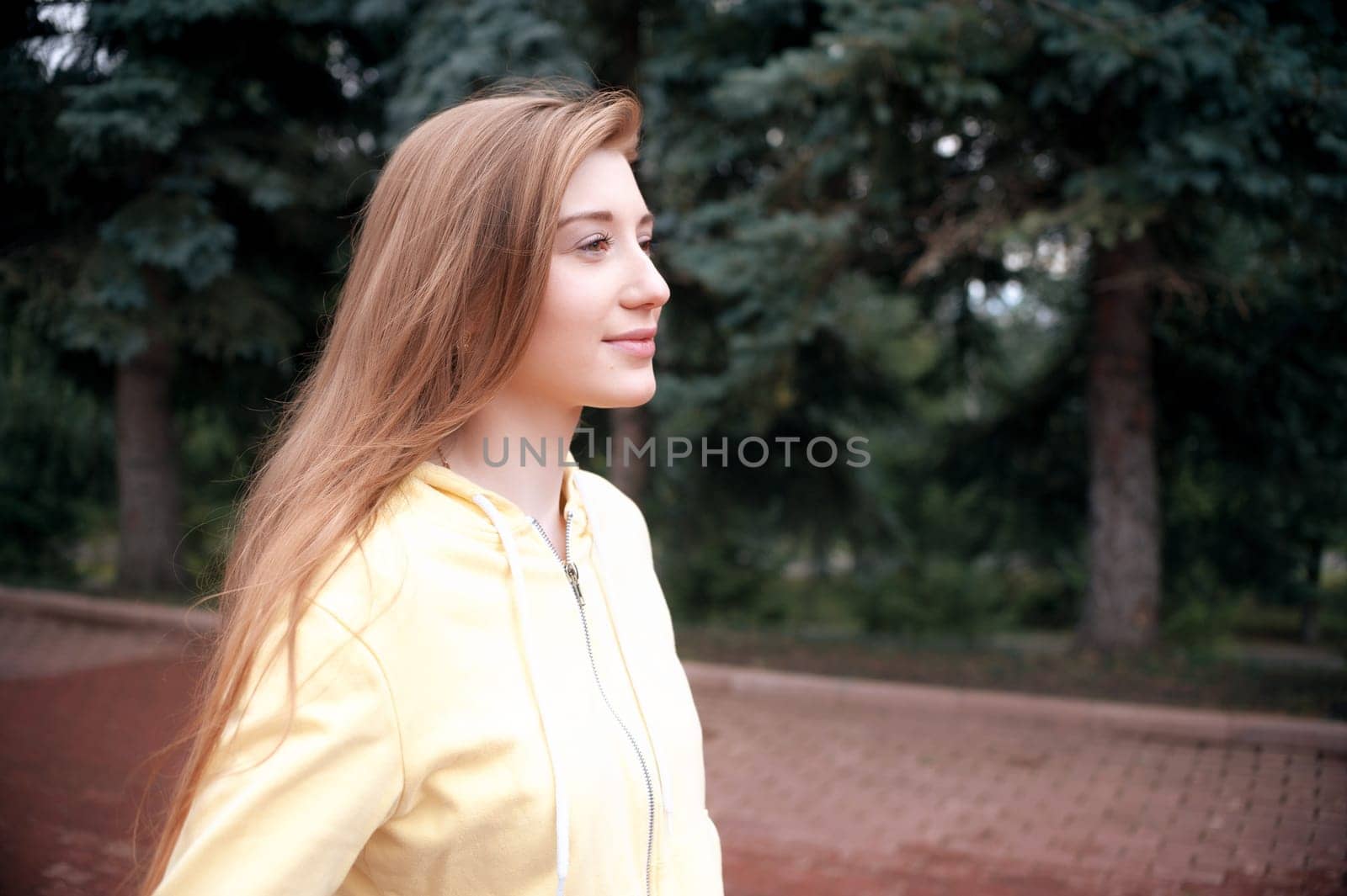 A pretty girl with long red hair, walks through the park and smiles. Portrait in the open air